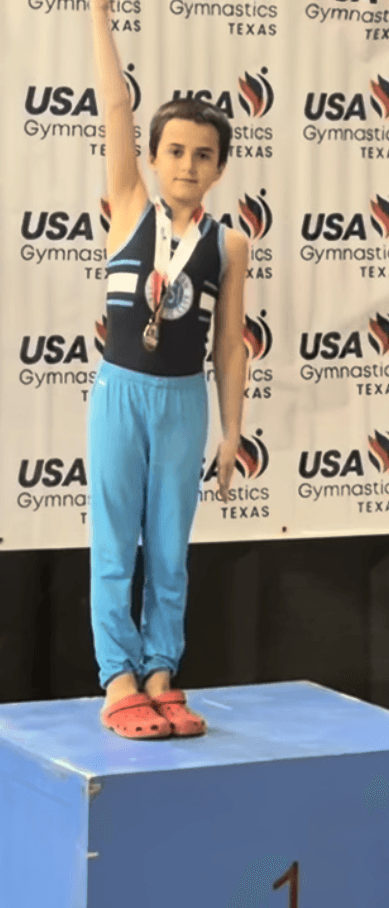 Lukas on the first-place podium at the Texas Level 6 State Championships, medal around his neck and one arm raised.